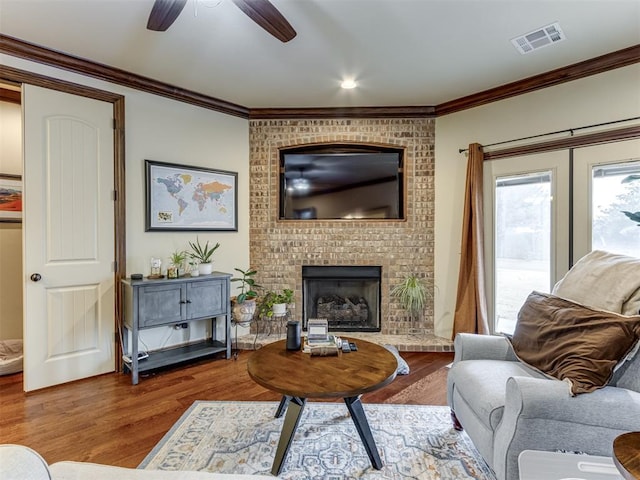 living room with wood-type flooring, ornamental molding, ceiling fan, and a fireplace