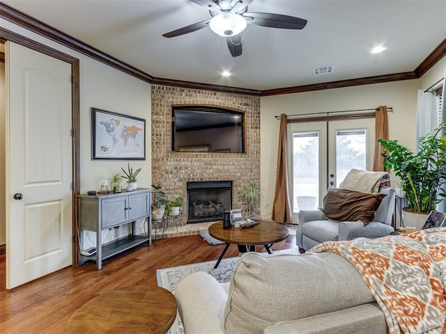 living room featuring hardwood / wood-style floors, a fireplace, ornamental molding, ceiling fan, and french doors