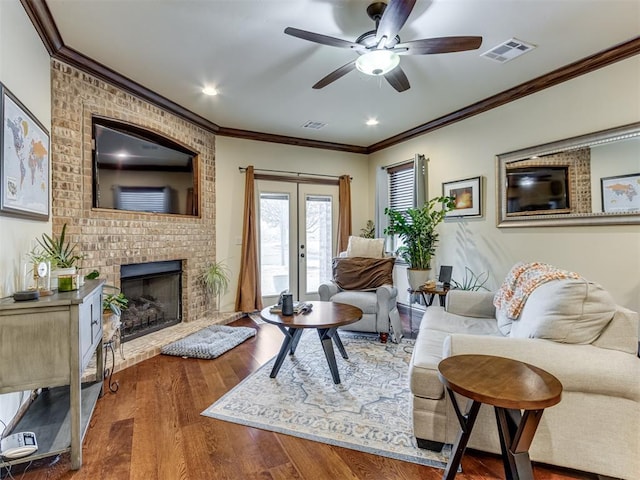 living room featuring crown molding, ceiling fan, a fireplace, wood-type flooring, and french doors