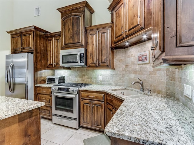 kitchen with sink, light stone counters, light tile patterned floors, appliances with stainless steel finishes, and backsplash