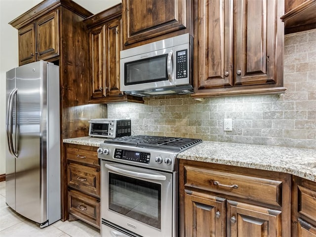kitchen featuring light stone counters, backsplash, light tile patterned flooring, and appliances with stainless steel finishes