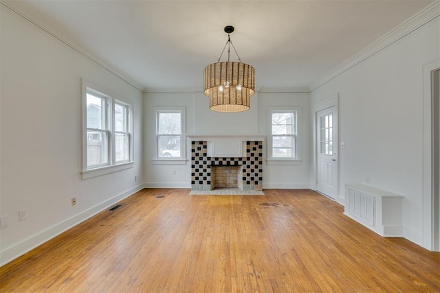 unfurnished living room featuring a tiled fireplace, ornamental molding, a healthy amount of sunlight, and light hardwood / wood-style flooring