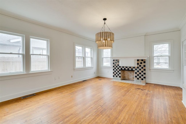 unfurnished living room with a chandelier, a tiled fireplace, and light wood-type flooring