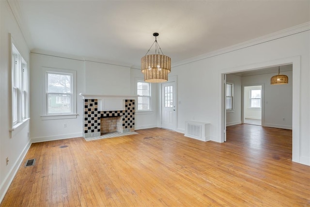 unfurnished living room featuring an inviting chandelier, ornamental molding, a tiled fireplace, and light hardwood / wood-style floors