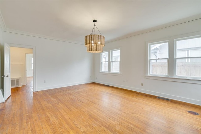 empty room with crown molding, a chandelier, and light wood-type flooring