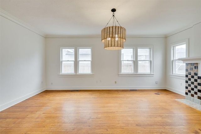 unfurnished room with a tiled fireplace, ornamental molding, a chandelier, and light hardwood / wood-style flooring