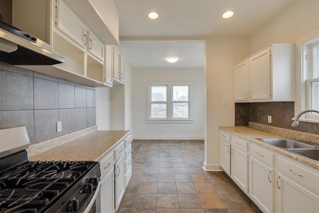 kitchen featuring backsplash, stainless steel range with gas stovetop, sink, and white cabinets