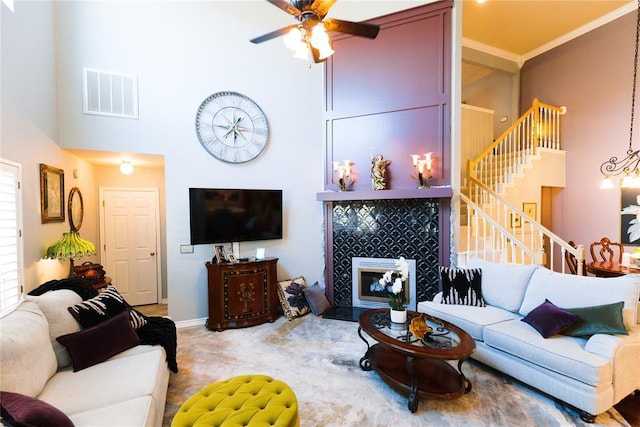 living room with visible vents, a towering ceiling, ceiling fan, a tile fireplace, and stairs