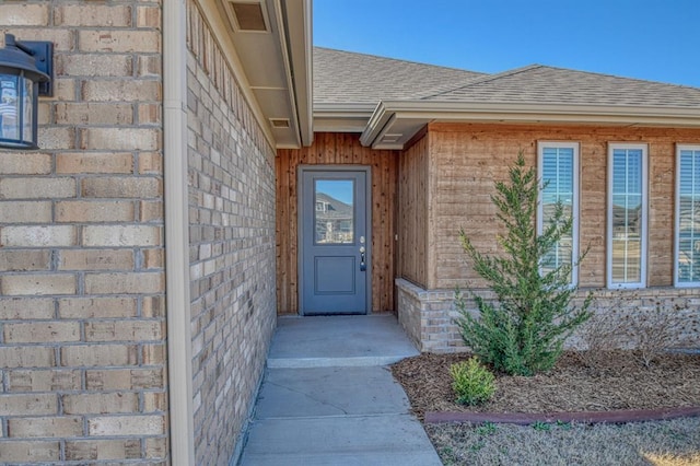 property entrance featuring brick siding and roof with shingles