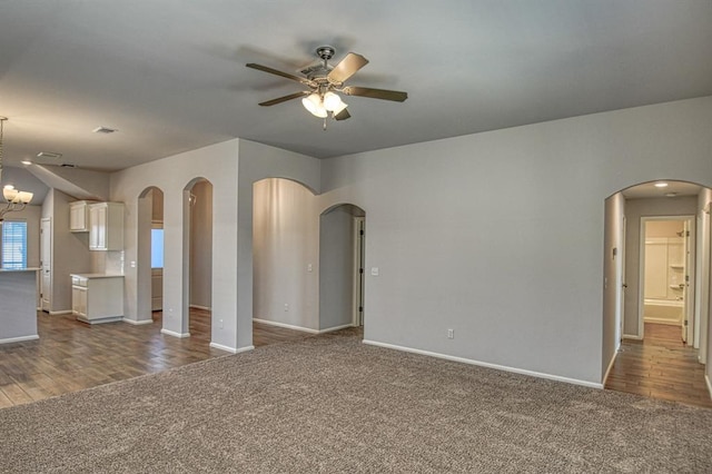 unfurnished living room featuring arched walkways, dark carpet, baseboards, and ceiling fan with notable chandelier