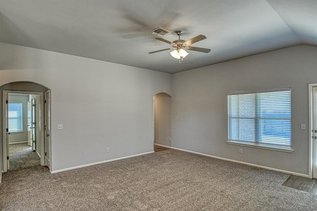 empty room featuring carpet floors, arched walkways, visible vents, and vaulted ceiling