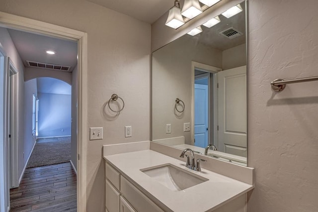 bathroom with a textured wall, vanity, wood finished floors, and visible vents