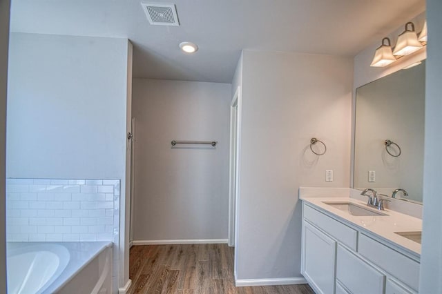 full bath featuring visible vents, a sink, wood finished floors, baseboards, and a bath