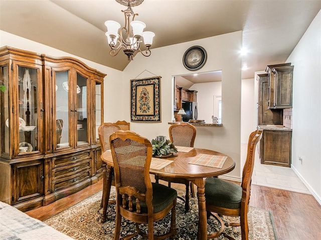 dining area featuring hardwood / wood-style flooring, an inviting chandelier, and vaulted ceiling