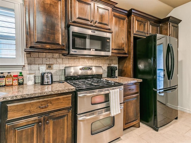 kitchen with light tile patterned floors, stainless steel appliances, tasteful backsplash, light stone countertops, and vaulted ceiling