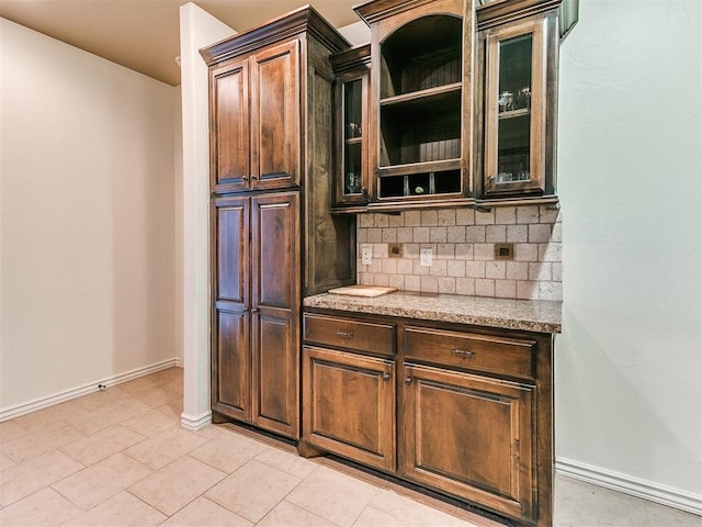 kitchen with tasteful backsplash, dark brown cabinets, light stone countertops, and light tile patterned flooring