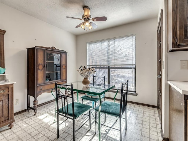 dining room with baseboards, ceiling fan, a textured ceiling, and light floors