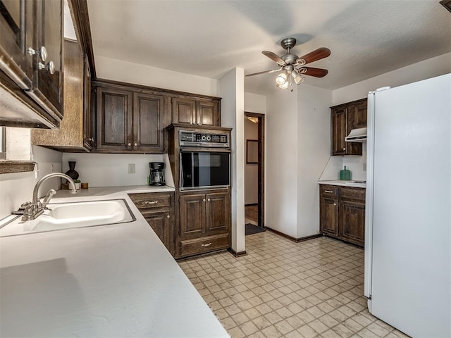 kitchen featuring oven, dark brown cabinets, a sink, and freestanding refrigerator