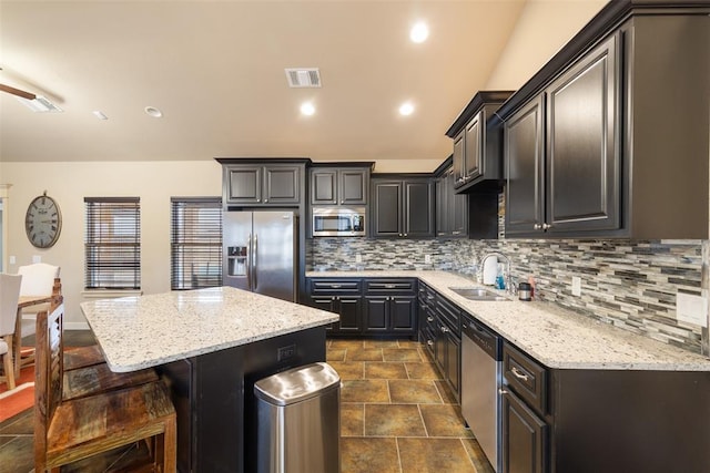 kitchen featuring sink, a breakfast bar area, stainless steel appliances, light stone countertops, and a kitchen island