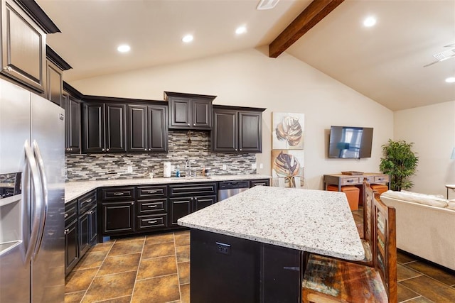 kitchen with appliances with stainless steel finishes, vaulted ceiling with beams, light stone counters, a center island, and backsplash