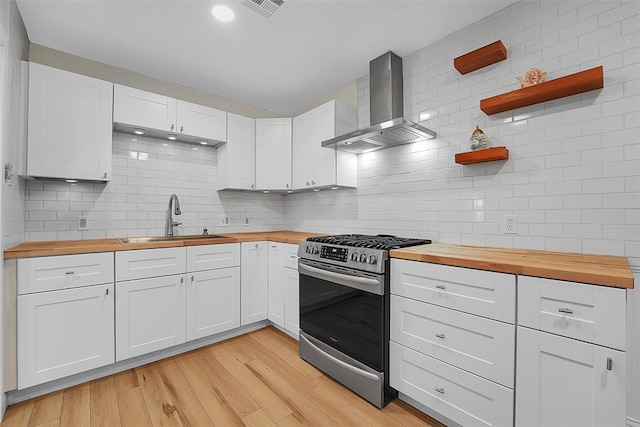 kitchen featuring white cabinets, gas range, wooden counters, and wall chimney exhaust hood