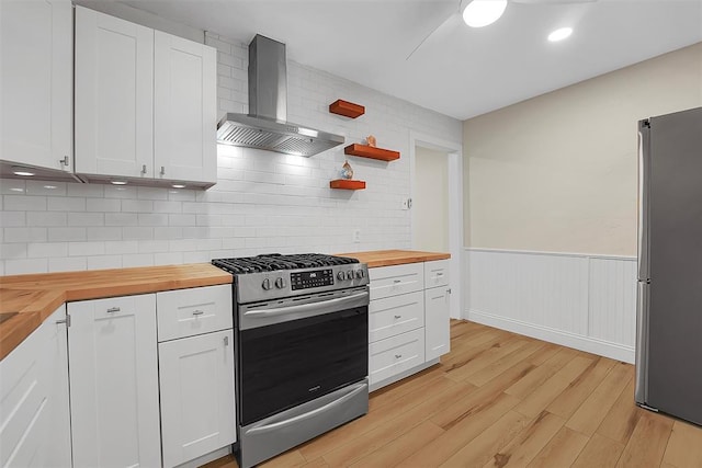 kitchen with light hardwood / wood-style flooring, wooden counters, appliances with stainless steel finishes, white cabinetry, and wall chimney exhaust hood