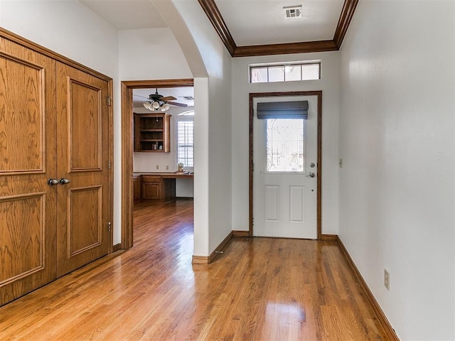 entrance foyer with visible vents, baseboards, ornamental molding, light wood-style flooring, and arched walkways