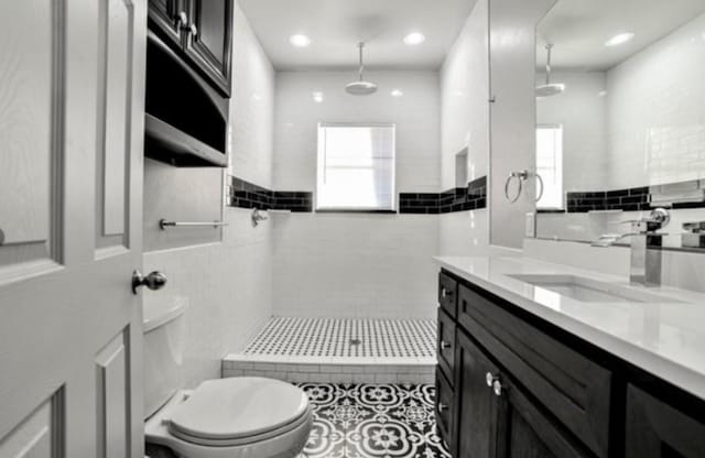 bathroom featuring vanity, tiled shower, tile walls, and toilet