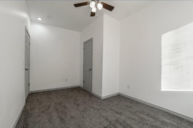 spare room featuring dark colored carpet and ceiling fan