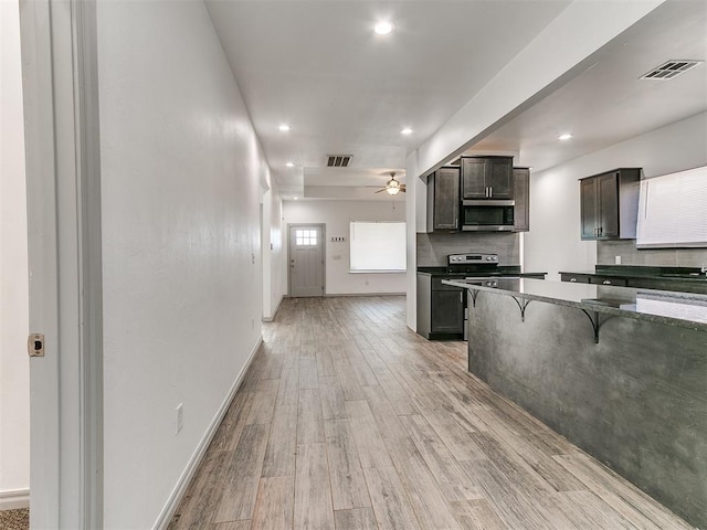 kitchen featuring visible vents, decorative backsplash, light wood-style flooring, stainless steel microwave, and a breakfast bar