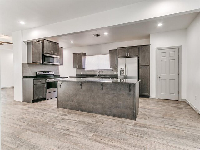 kitchen with a center island, light wood-style flooring, appliances with stainless steel finishes, dark brown cabinets, and a kitchen bar