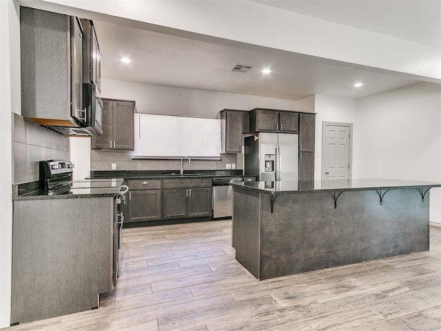 kitchen featuring light wood finished floors, stainless steel appliances, a breakfast bar, and visible vents