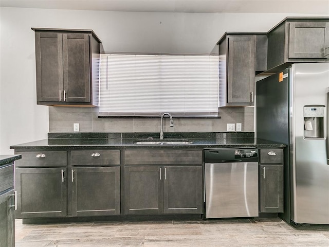 kitchen with appliances with stainless steel finishes, a sink, dark stone countertops, dark brown cabinets, and light wood-type flooring