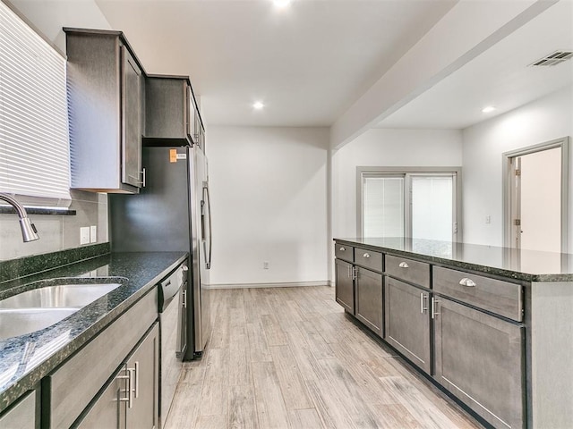 kitchen featuring light wood finished floors, stainless steel dishwasher, dark stone countertops, and visible vents