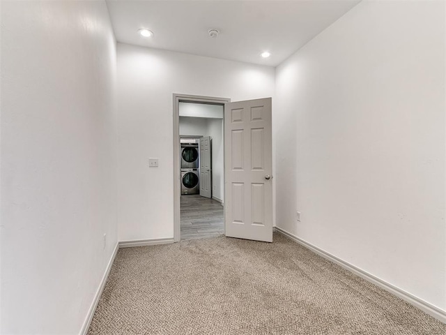 empty room featuring stacked washer and dryer, recessed lighting, carpet flooring, and baseboards