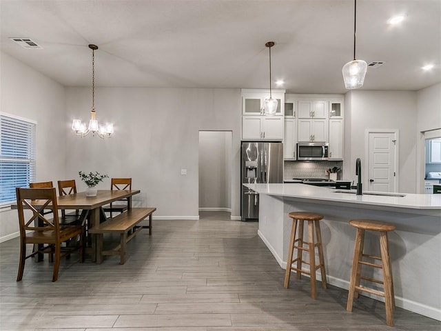 kitchen featuring decorative light fixtures, sink, white cabinets, stainless steel appliances, and light wood-type flooring