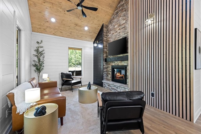 living room with a stone fireplace, high vaulted ceiling, ceiling fan, wooden ceiling, and light hardwood / wood-style flooring