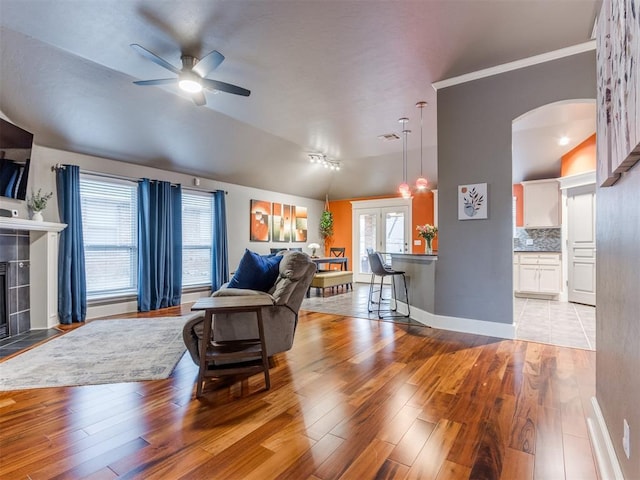 living room featuring ceiling fan, light hardwood / wood-style floors, vaulted ceiling, and a tile fireplace