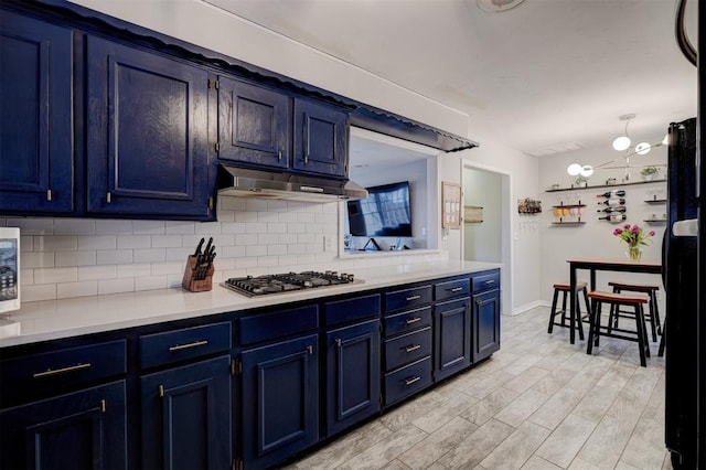 kitchen featuring stainless steel gas stovetop, blue cabinetry, black refrigerator, and decorative backsplash