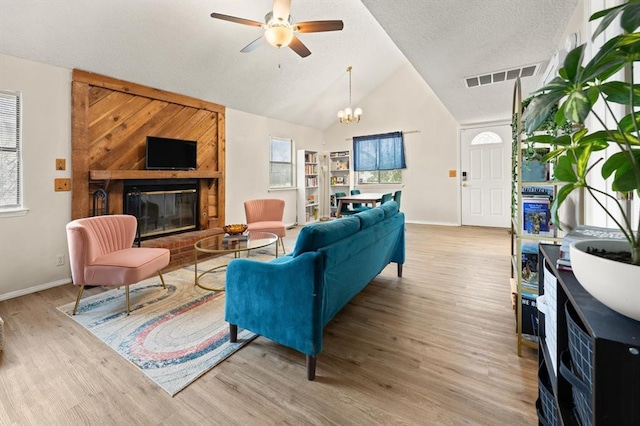 living room with high vaulted ceiling, light hardwood / wood-style flooring, a textured ceiling, a fireplace, and ceiling fan with notable chandelier