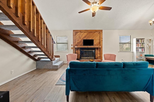 living room featuring vaulted ceiling, a fireplace, hardwood / wood-style flooring, ceiling fan, and a textured ceiling