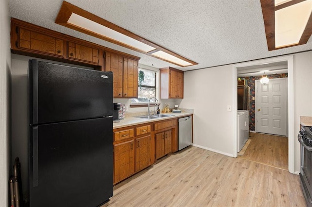 kitchen with black refrigerator, dishwasher, sink, a textured ceiling, and light hardwood / wood-style flooring