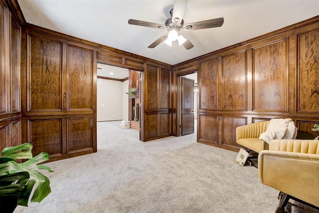 sitting room with a ceiling fan, wood walls, crown molding, a decorative wall, and light colored carpet