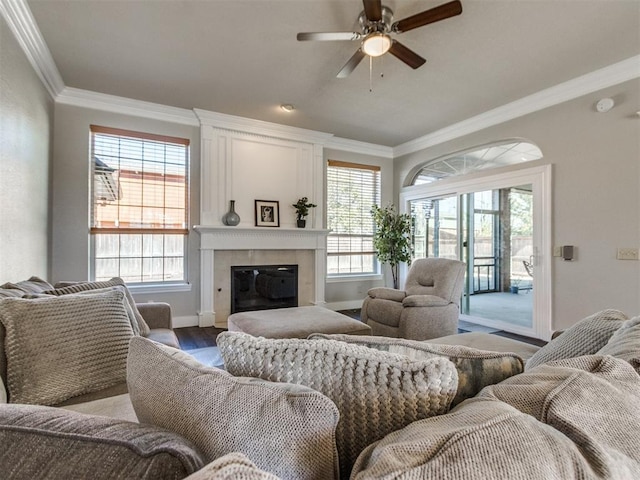 living room featuring a fireplace, ornamental molding, light wood-style floors, a ceiling fan, and baseboards