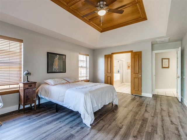 bedroom featuring ensuite bathroom, wood finished floors, a raised ceiling, and baseboards