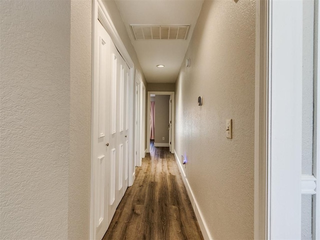 hall with dark wood-type flooring, visible vents, a textured wall, and baseboards