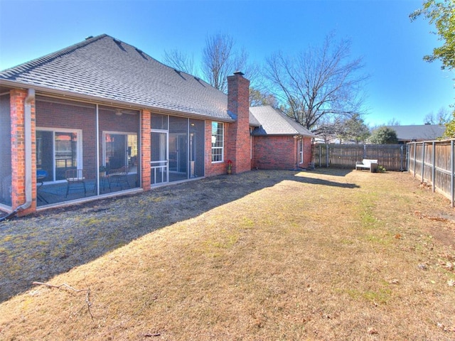 back of house with a shingled roof, a sunroom, a fenced backyard, a yard, and brick siding