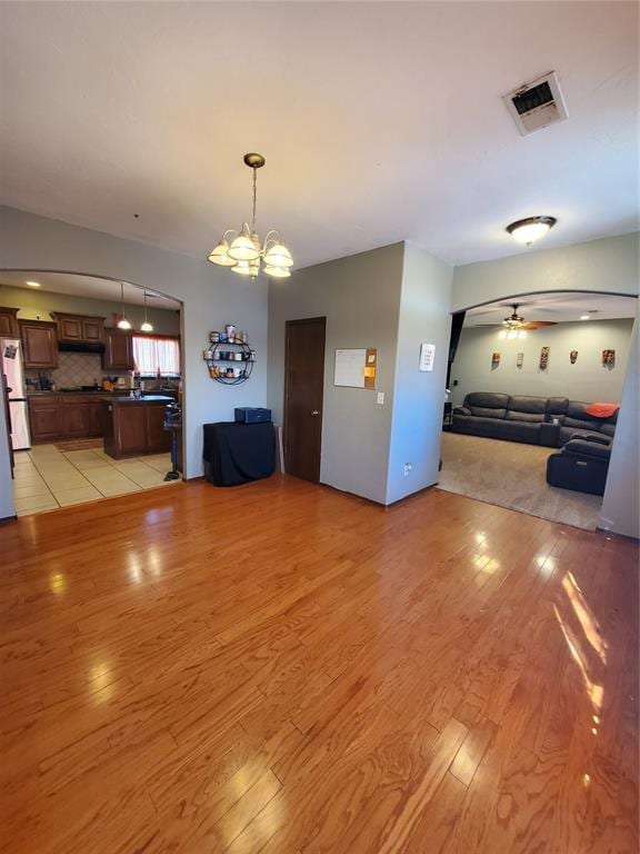 unfurnished living room featuring ceiling fan with notable chandelier and light wood-type flooring