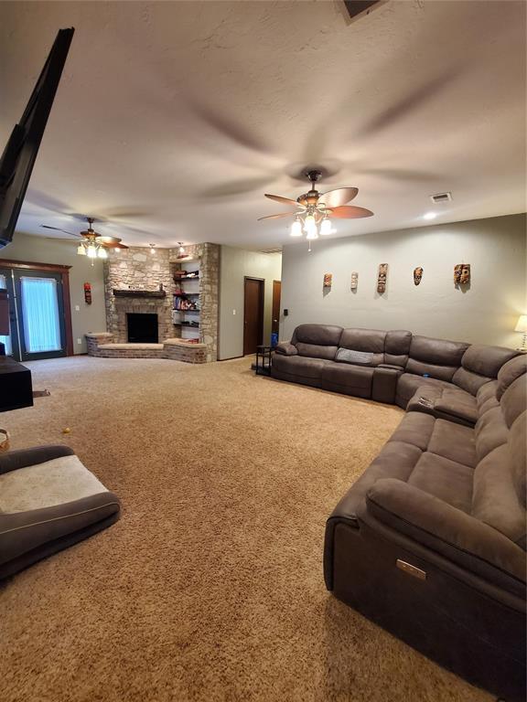 carpeted living room featuring a stone fireplace and ceiling fan