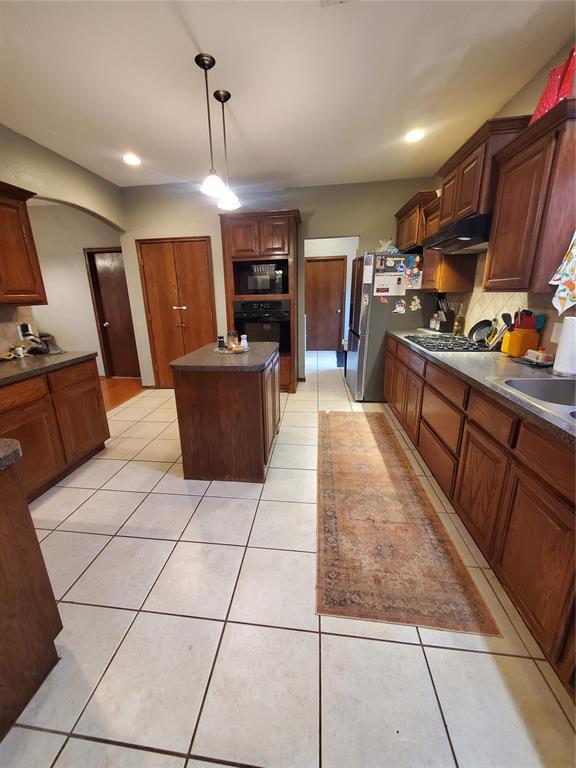 kitchen with light tile patterned flooring, sink, backsplash, a center island, and stainless steel appliances